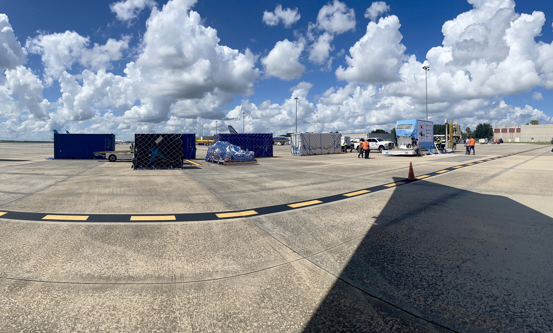 An image of the KPLO shipping container being transported between the B-747 aircraft and the Orlando International Airport.